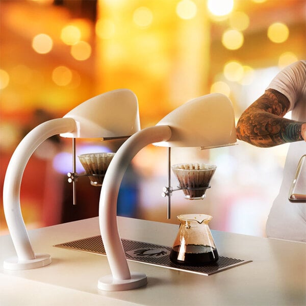 A man using a Curtis Seraphim single cup coffee brewer to pour coffee into a glass container.