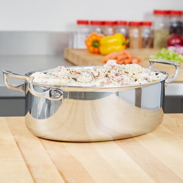 A silver Vollrath oval au gratin with food inside on a wooden surface.