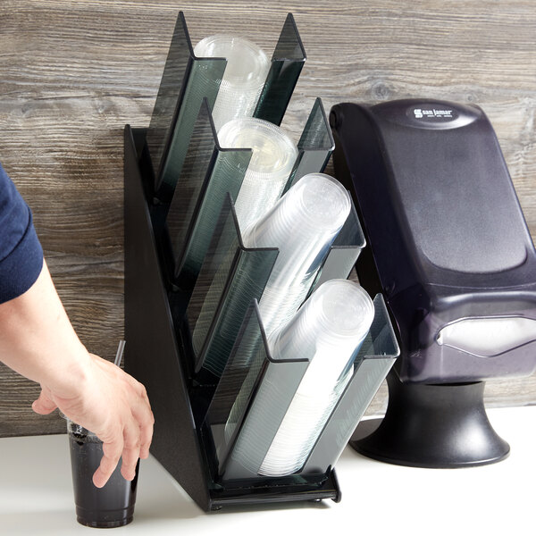 A person holding a cup and a straw using a black plastic Vollrath countertop organizer.