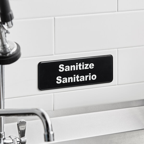 A black and white Tablecraft sign that says "Sanitario" and "Sanitario"