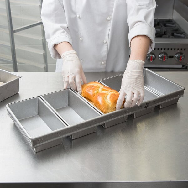 A person in gloves putting a loaf of bread into a Chicago Metallic aluminized steel bread loaf pan.