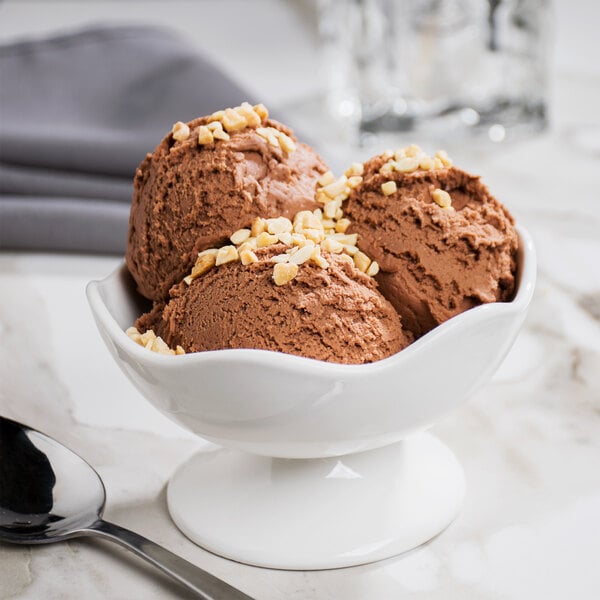 A white 10 Strawberry Street Whittier wavy footed bowl filled with chocolate ice cream topped with nuts.