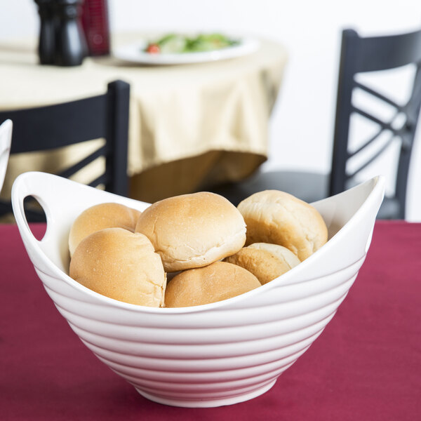 A white porcelain boat bowl filled with rolls on a table.