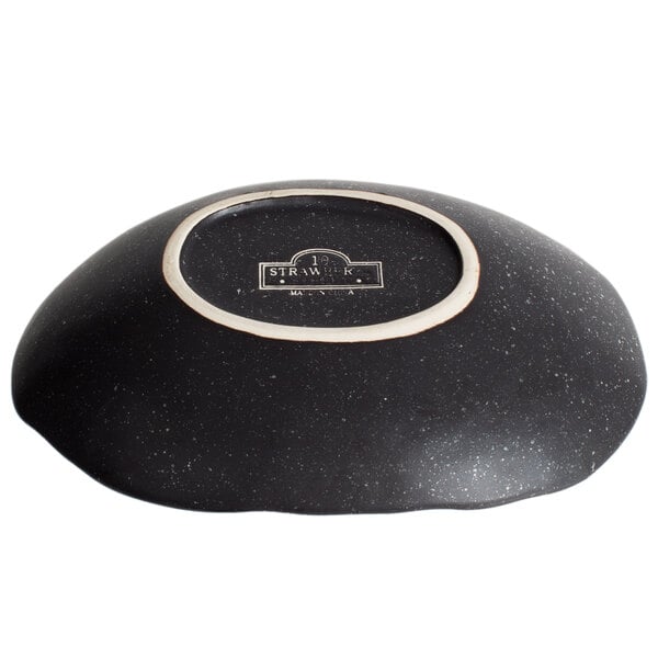 A close-up of a black oval stoneware bowl with a white rim.