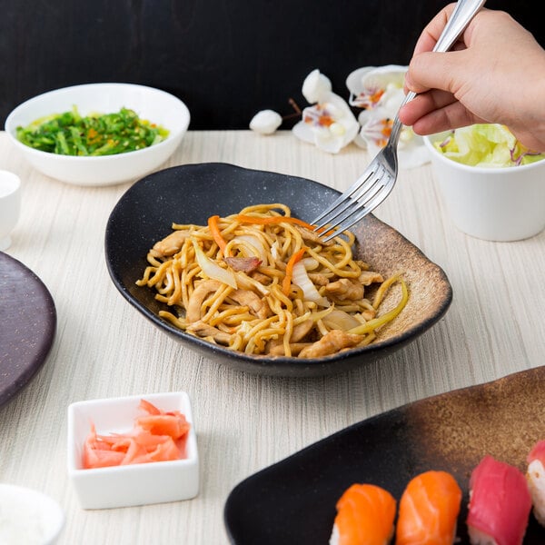 A white oval stoneware bowl with noodles, lettuce, and vegetables on a table.
