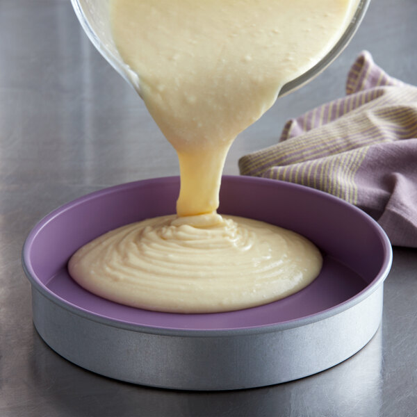 A person pouring white cake batter into a Chicago Metallic round cake pan.