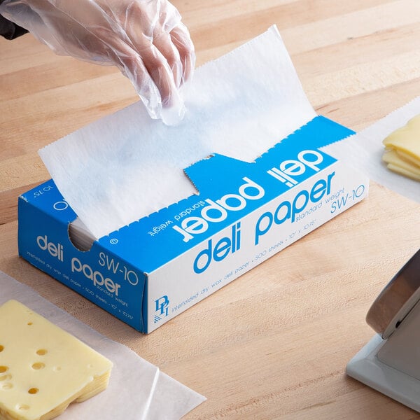 A hand in a plastic glove using Durable Packaging deli wax paper to cut cheese.