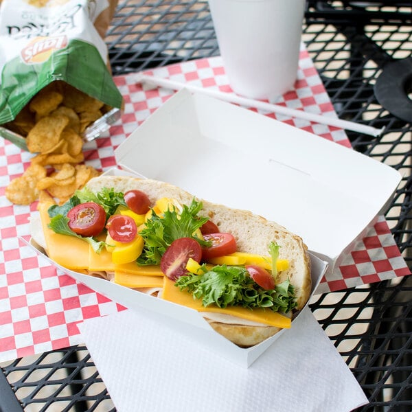 A white paper sandwich container holding a sandwich with cheese and tomatoes.