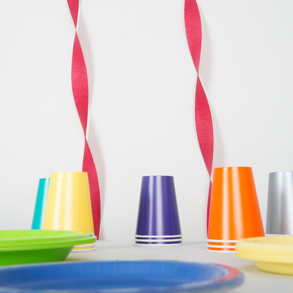 Burgundy streamer paper on a table with colorful cups and plates.