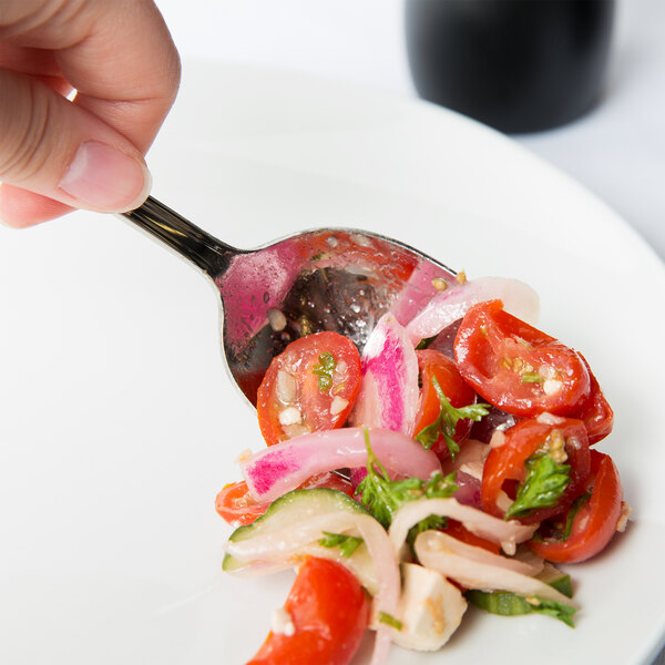 A hand holding a Libbey stainless steel serving spoon over a salad.