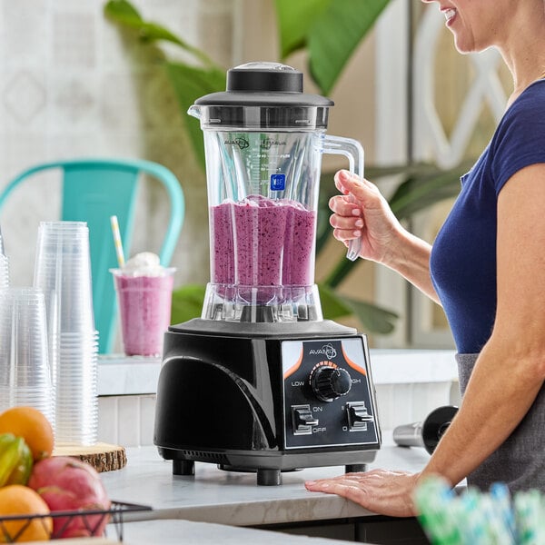 A commercial blender with a clear container filled with a purple smoothie, operated by a person in a kitchen setting.