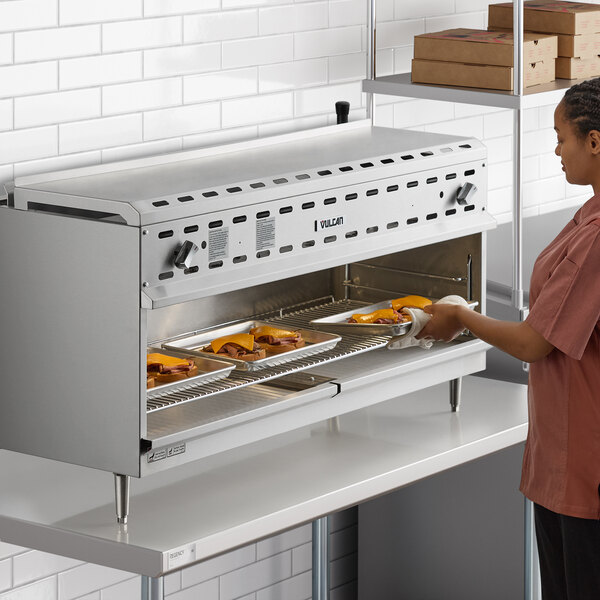 A woman putting food into a Vulcan cheese melter.