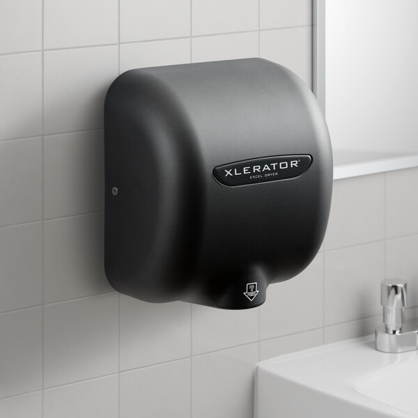 A graphite XLERATOR hand dryer on a white tile wall above a white sink.