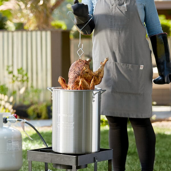 chef wearing heat protective gloves pulling a deep fried turkey out of an outdoor fryer pot