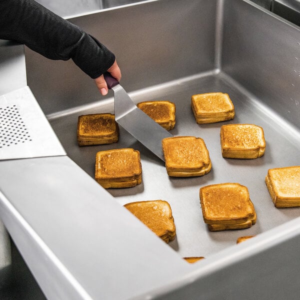 A person cutting toasted sandwiches in a Vulcan tilt skillet.