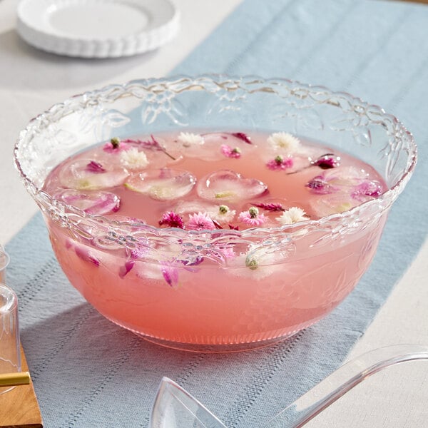 A clear plastic punch bowl with a floral design, filled with pink punch and floating flowers.