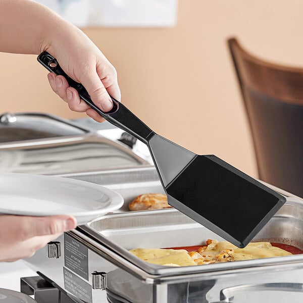 A person holding a black Cambro solid turner over a plate of food.