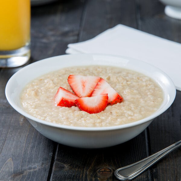 A white porcelain cereal bowl filled with oatmeal and strawberries.