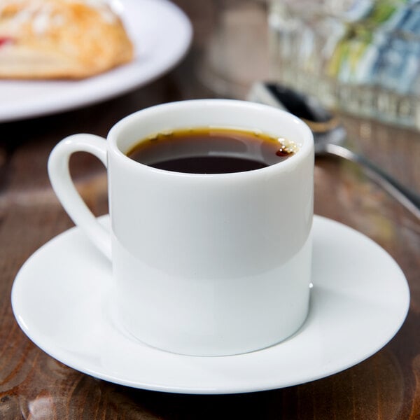 A white 10 Strawberry Street porcelain espresso cup full of brown coffee on a saucer.