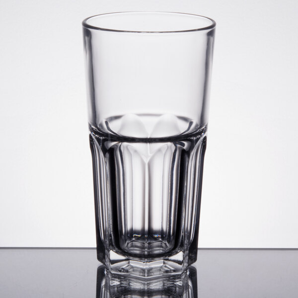 An Arcoroc stackable beverage glass filled with a clear liquid on a table.