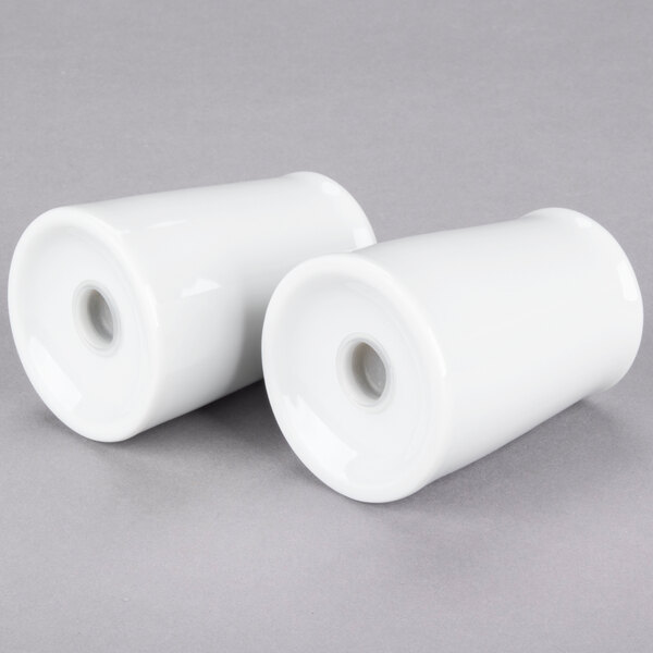 A close-up of two white cylindrical porcelain cups.