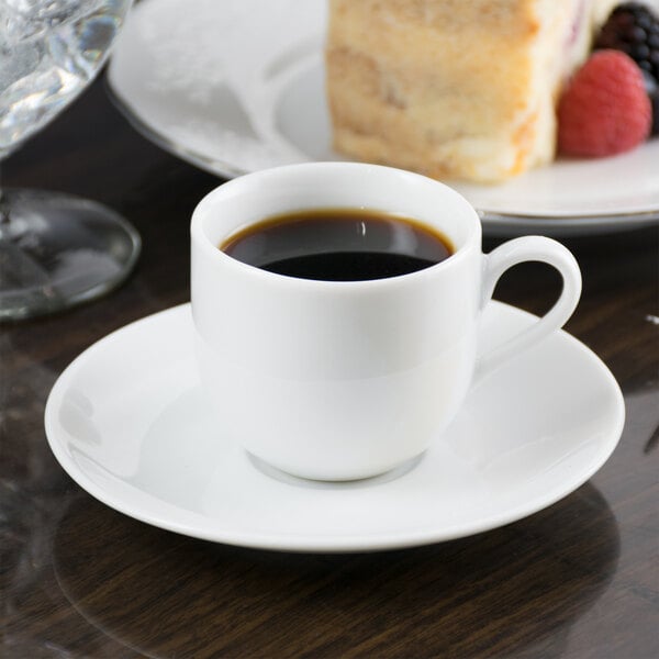 A 10 Strawberry Street white porcelain espresso cup on a saucer with a cup of coffee and a plate of cake.