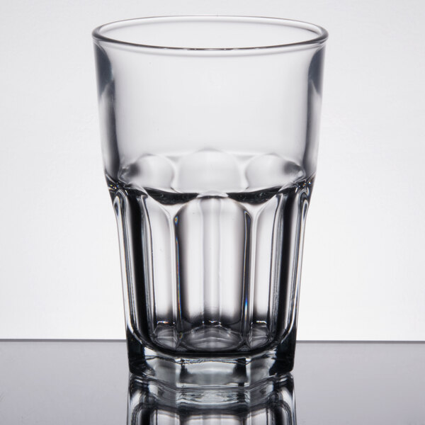 A close up of a clear Arcoroc stackable cooler glass with a few drops of water inside.