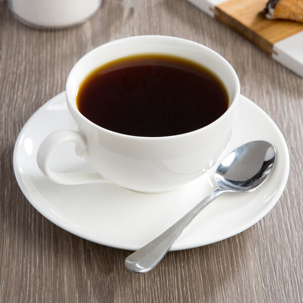 A 10 Strawberry Street white porcelain coffee cup on a saucer with a spoon.