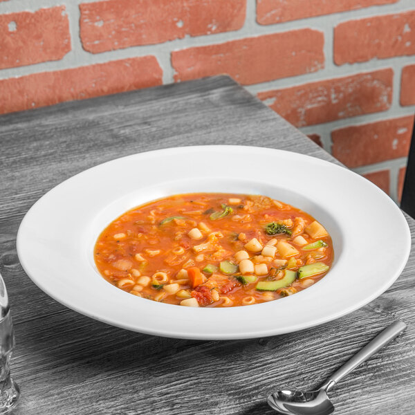 A 10 Strawberry Street Classic White porcelain soup bowl filled with soup and vegetables with a spoon on a table.