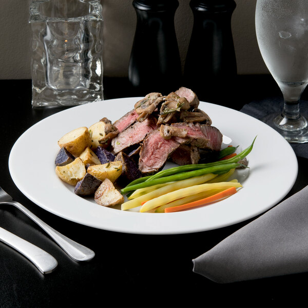 A close-up of a 10 Strawberry Street Classic White porcelain dinner plate with meat and vegetables and silverware.