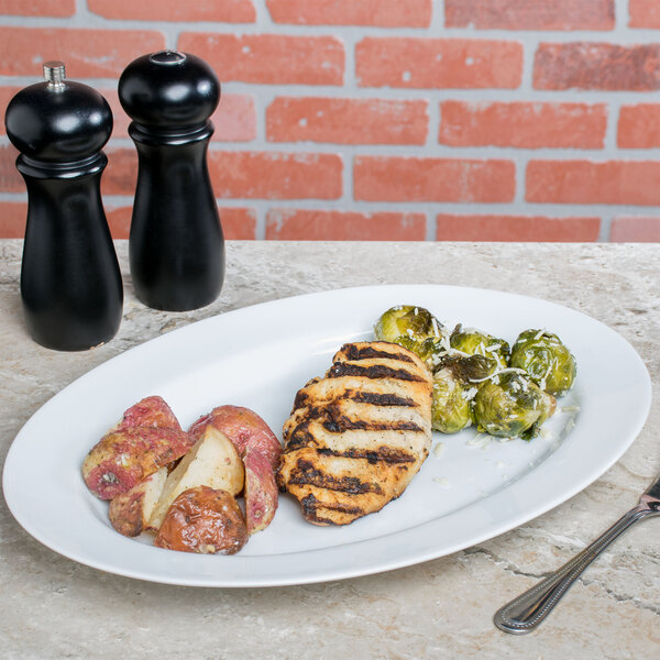 A 10 Strawberry Street white porcelain oval platter with chicken, potatoes, and vegetables on it.