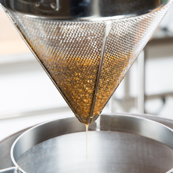 A metal Vollrath fine china cap strainer pouring brown liquid through a metal funnel.