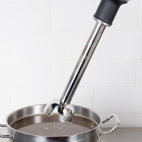 A hand using a KitchenAid KHBC112MSS blending arm to blend liquid in a pot.
