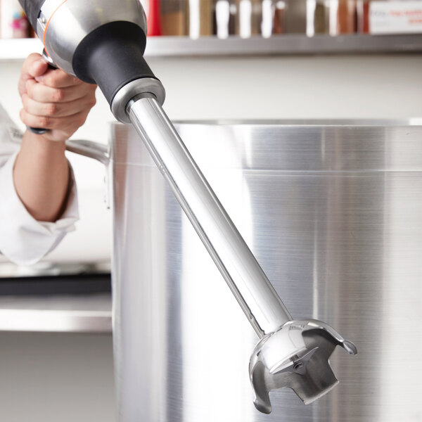 A hand holding a KitchenAid 400 Series immersion blender over a large pot.