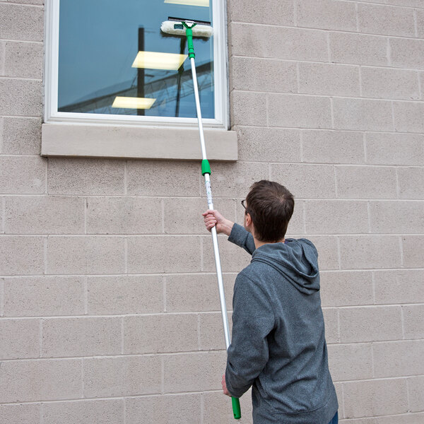 A man using an Unger telescopic pole to clean a window.