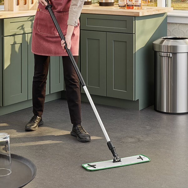 A woman in an apron using a Lavex microfiber mop to clean a professional kitchen floor.