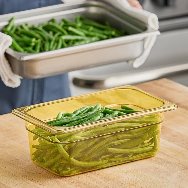 A person holding a Cambro plastic food pan filled with green beans.