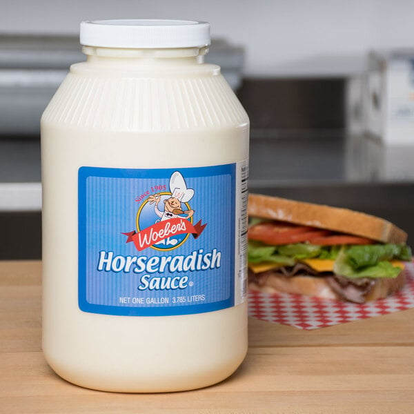 A white bottle of Woeber's Horseradish Sauce on a table next to a sandwich.