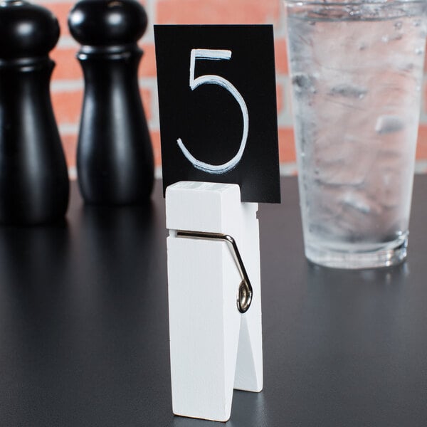 An American Metalcraft white clothespin card holder with a number on a table.