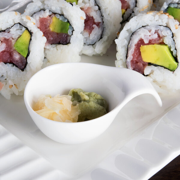 A plate of sushi with a white porcelain spoon of sauce on the side.