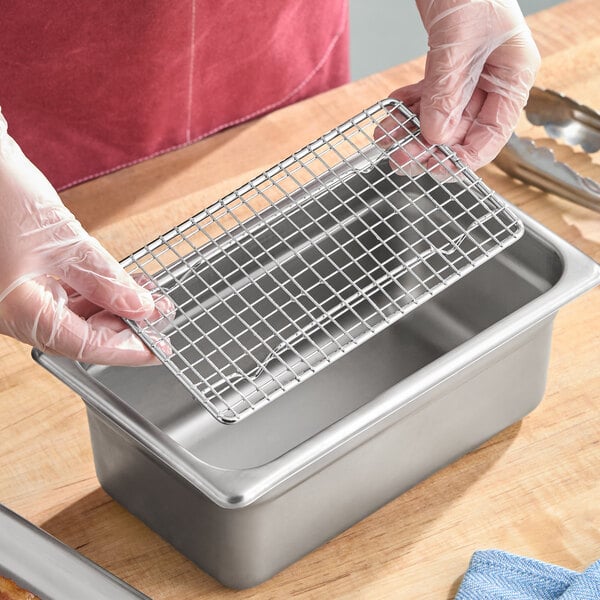 A rectangular metal footed pan grate being placed into a stainless steel steam table pan.