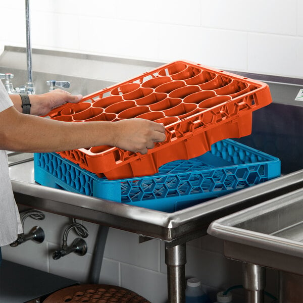 A person using a Carlisle orange and blue glass rack extender to wash dishes in a sink.