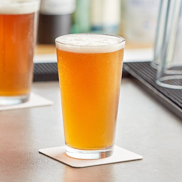 Two Acopa Select rim tempered pint glasses of beer on a bar counter.