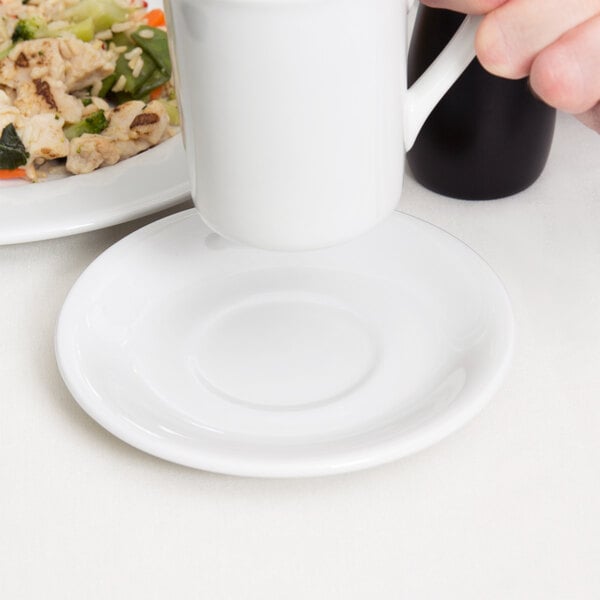 A hand holding a white Tuxton Alaska coupe saucer under a white mug.