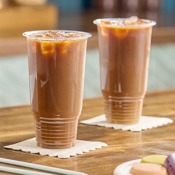 Two Choice clear plastic cups of iced coffee on a wooden table.