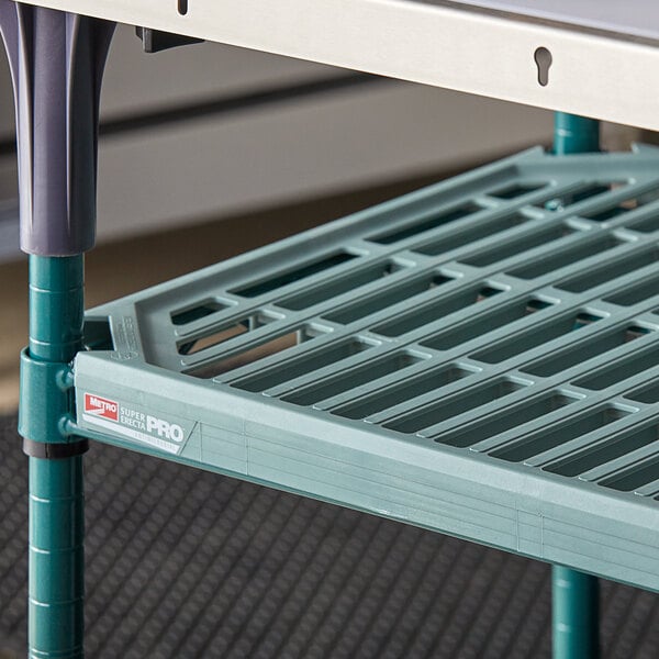 A green Metro Super Erecta wire shelf on a metal frame under a table in a professional kitchen.