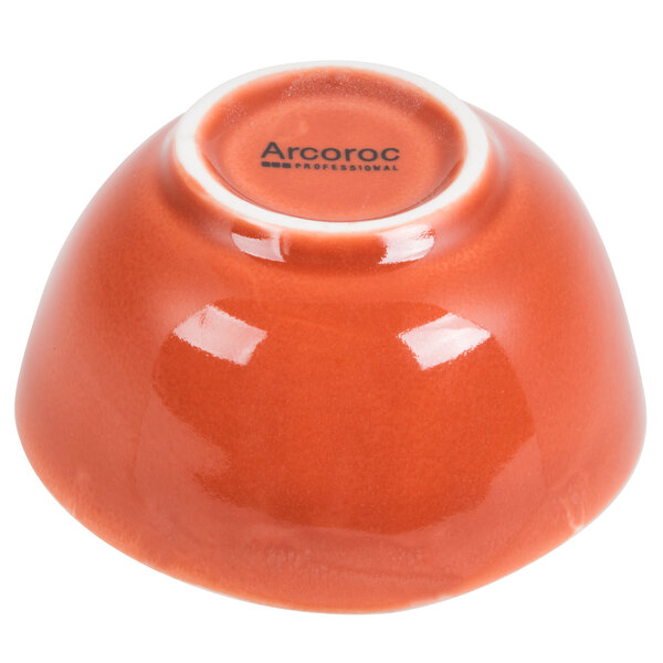 An orange porcelain bowl with the word "Arcoroc" on it.