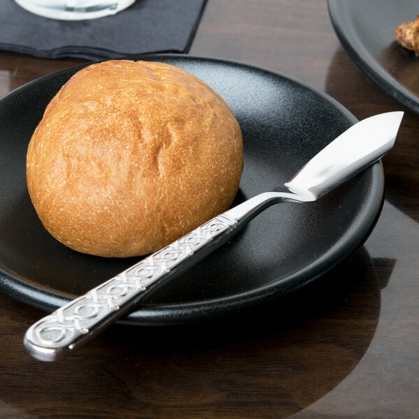 A black plate with a piece of round brown bread and a 10 Strawberry Street Dubai stainless steel butter knife.