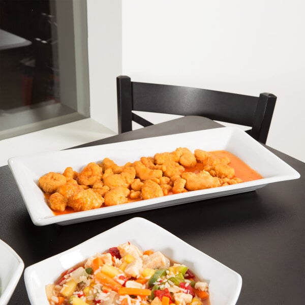 A white American Metalcraft rectangular stoneware platter with three plates of food on a table.