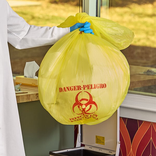 A person in a lab coat holding a yellow infectious linen and medical waste bag with a biohazard symbol.